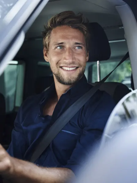 Mann sitzt lächelnd am Steuer eines Firmenwagens. 