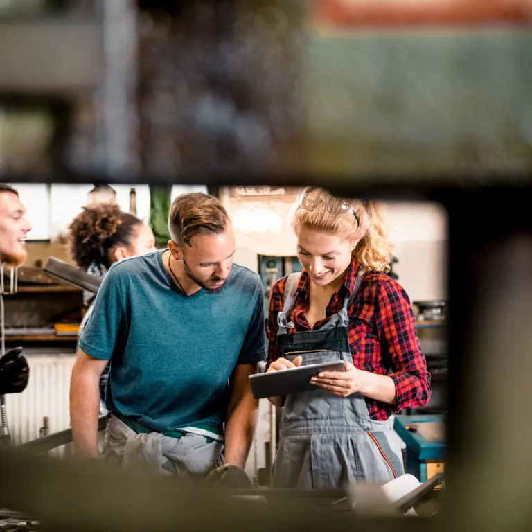Eine Gruppe Handwerker steht in einer Werkstatt und schaut auf ein Tablet. 