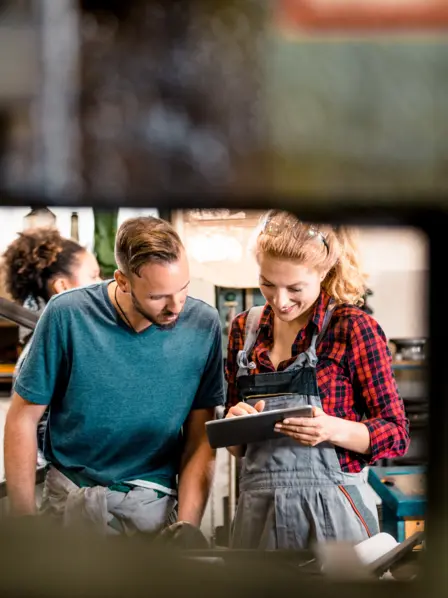 Eine Gruppe Handwerker steht in einer Werkstatt und schaut auf ein Tablet. 