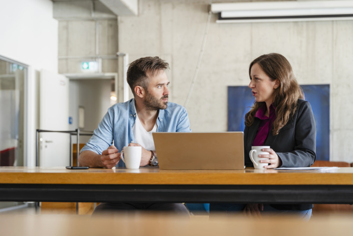 Arbeitnehmer sitzt im Gespräch mit einer Führungskraft an einem Tisch. 