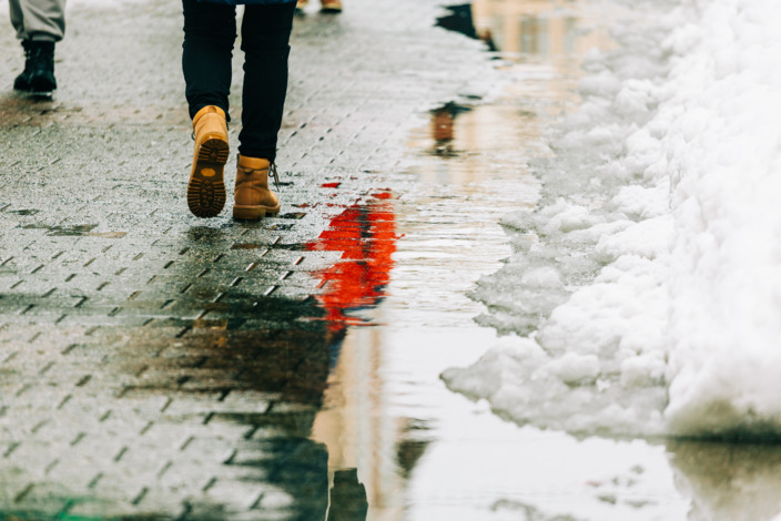 Fußgängerzone mit Menschen die auf einem mit Schnee bedeckten, nassen und glatten Weg laufen. 
