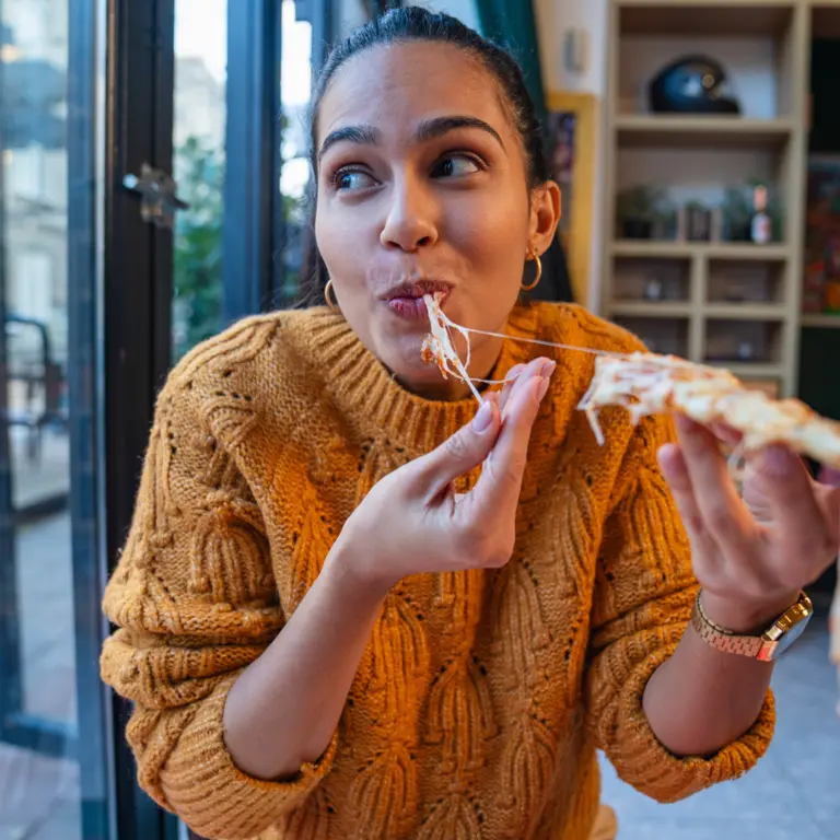 Frau beißt genüsslich in ein Stück Pizza.