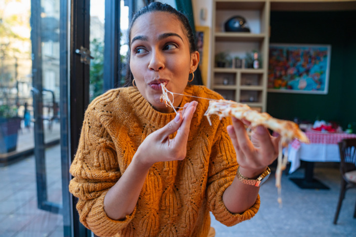 Frau sitzt im Restaurant und beißt genüßlich von einem Stück Pizza ab. 