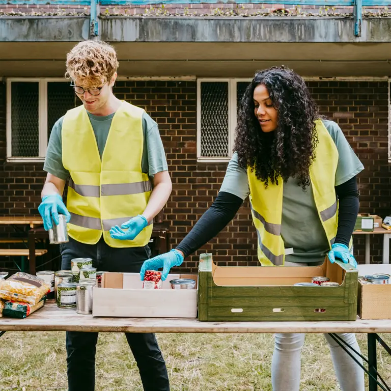 Zwei Arbeiter in Warnweste sortieren Lebensmittel.