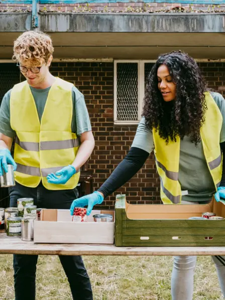 Zwei Arbeiter in Warnweste sortieren Lebensmittel.