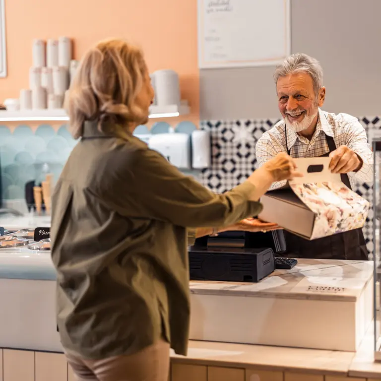 Älterer Mitarbeiter eines Cafes bedient eine Kundin.