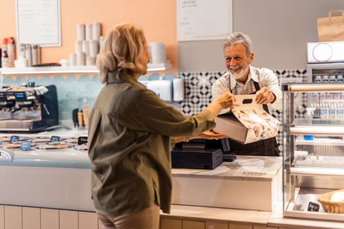 Älterer Mitarbeiter eines Cafes bedient eine Kundin.