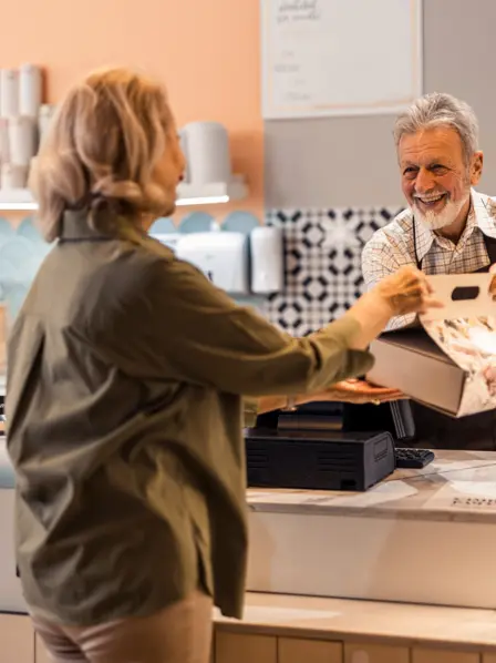Älterer Mitarbeiter eines Cafes bedient eine Kundin.