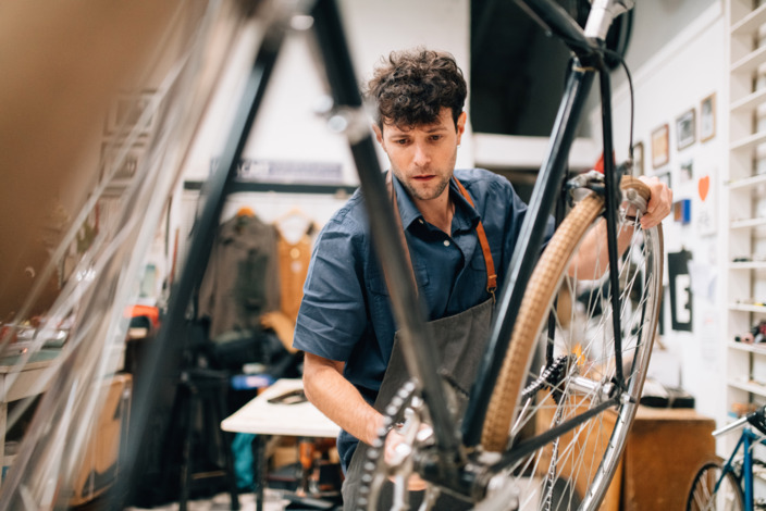 Mann steht in der Werkstatt und repariert ein Fahrrad.