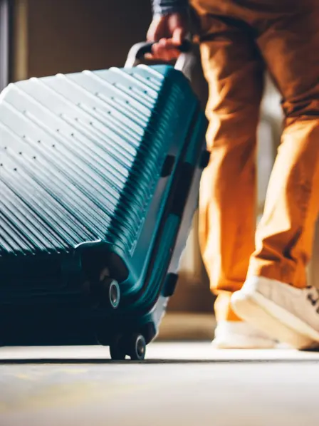 Mann rollt einen blauen Reisekoffer.