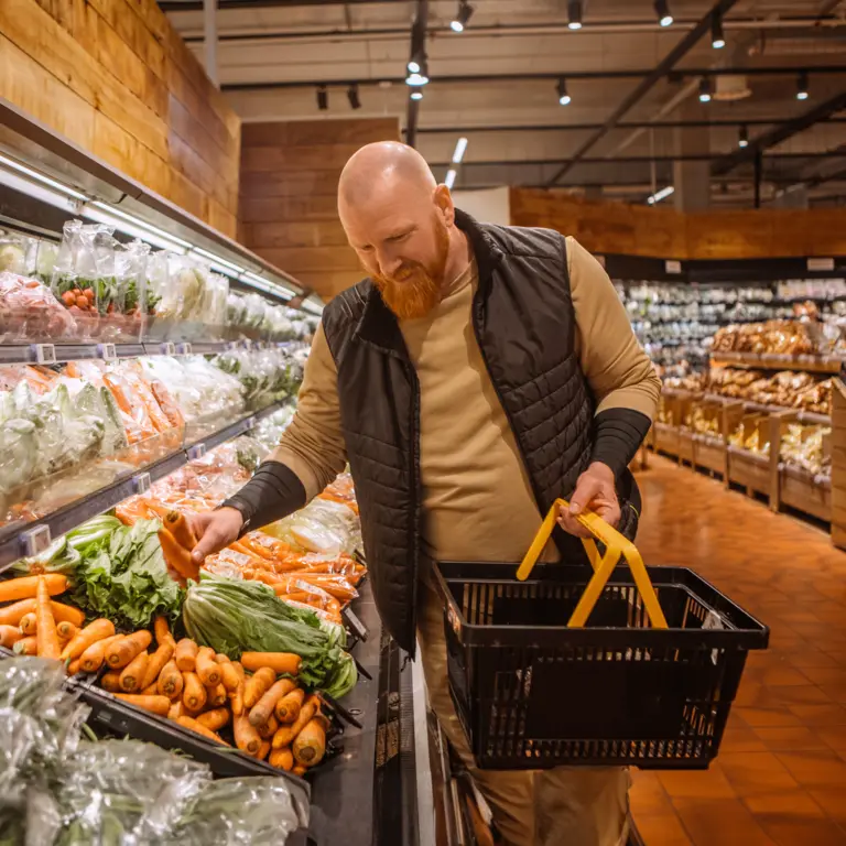 Mann steht im Supermarkt  in der Gemüseabteilung.