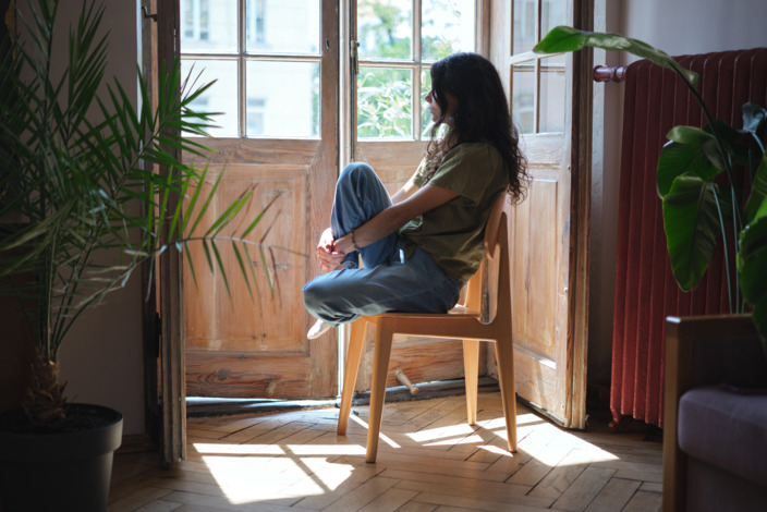 Eine Frau sitzt in einem Zimmer auf dem Stuhl und schaut nachdenklich aus dem Fenster. 