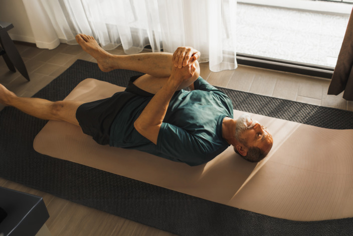 Mann liegt auf seiner Sportmatte und dehnt sich.