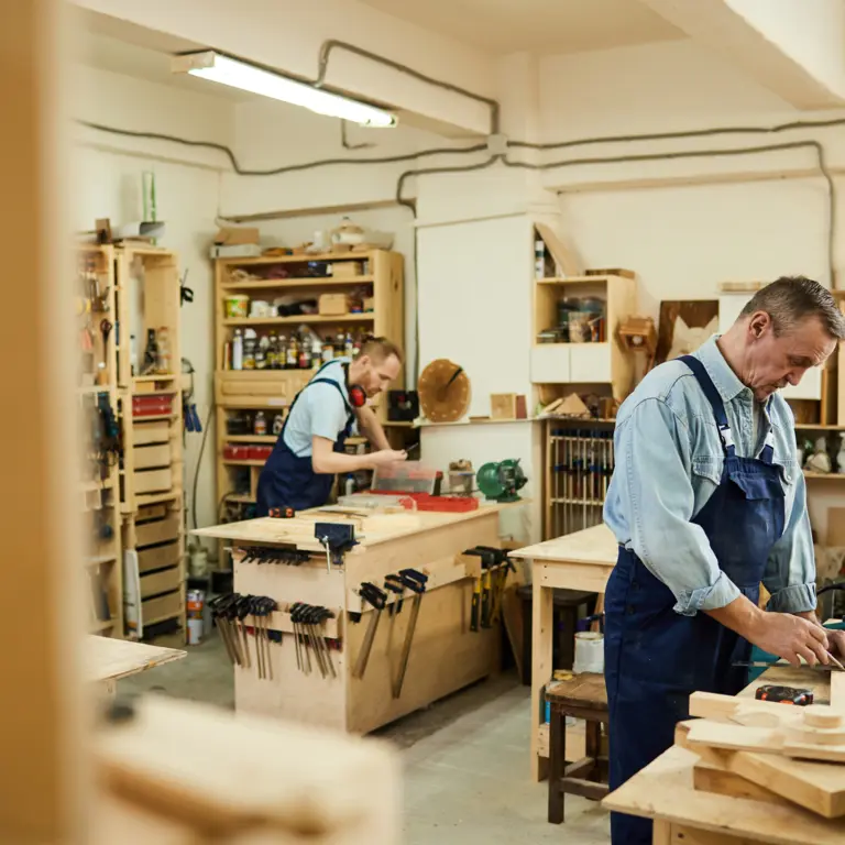 Zwei Handwerker arbeiten gemeinsam mit Holz in einer Werkstatt.