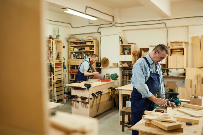 Zwei Handwerker arbeiten gemeinsam mit Holz in einer Werkstatt.