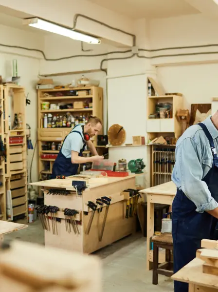 Zwei Handwerker arbeiten gemeinsam mit Holz in einer Werkstatt.