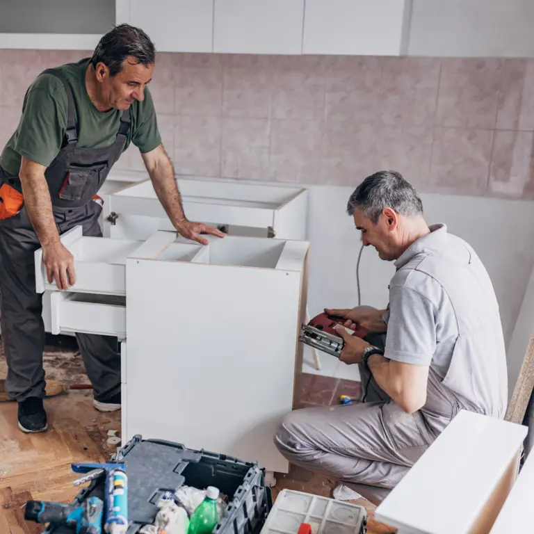 Zwei ältere Handwerker montieren Schränke in einer Küche.