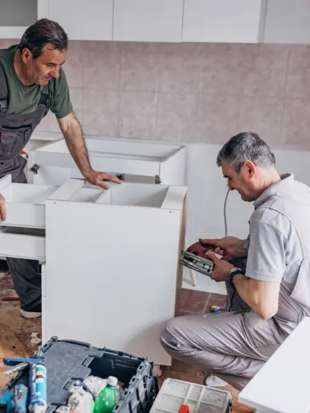 Zwei ältere Handwerker montieren Schränke in einer Küche.
