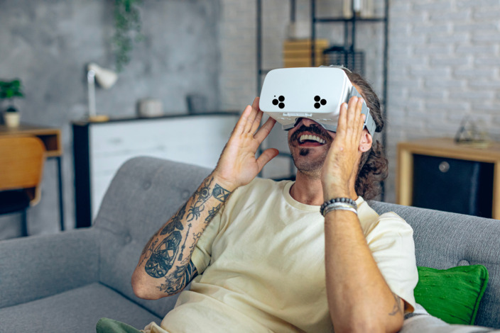Mann sitzt auf einer Couch und hat eine VR-Brille auf dem Kopf.