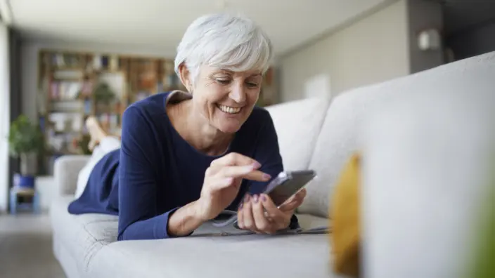 Frau liegt auf dem Sofa und nutzt die myReha App.