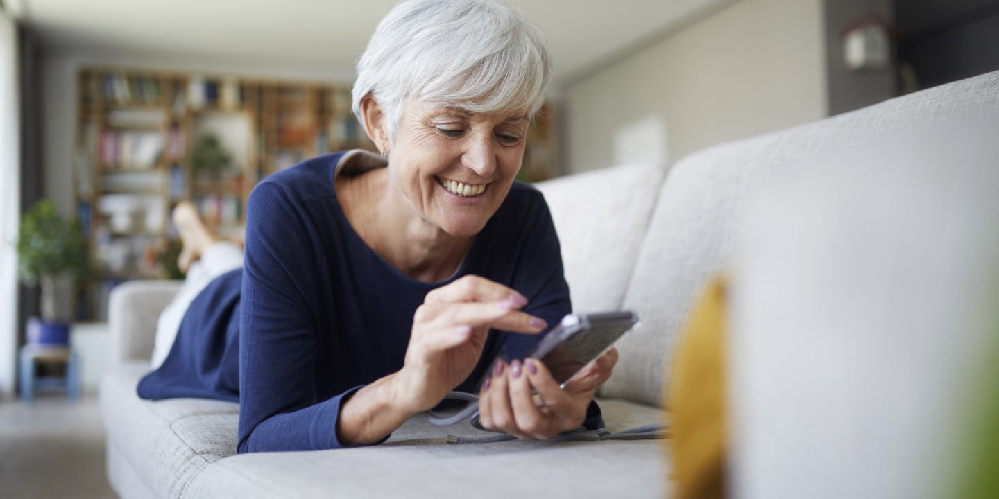 Frau sitzt auf dem Sofa und schaut auf ihr Smartphone.
