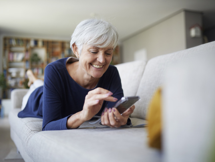 Frau liegt auf dem Sofa und nutzt die myReha App.