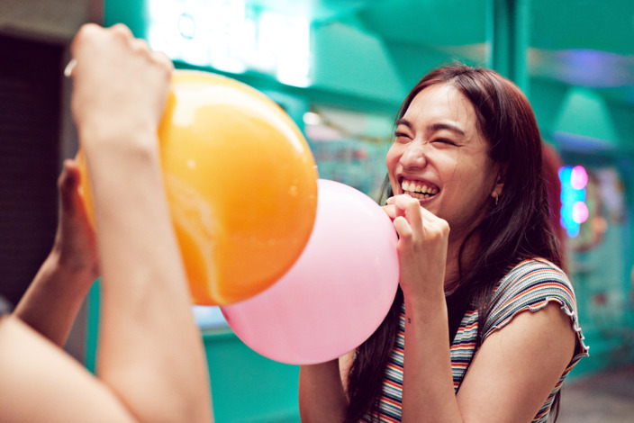Junge Frau lacht und hält einen Luftballon in der Hand
