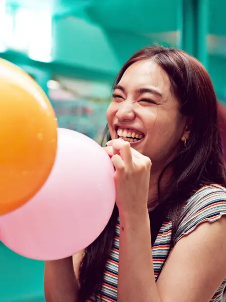 Frau hält Luftballon zum Inhalieren von Lachgas in den Händen und lacht
