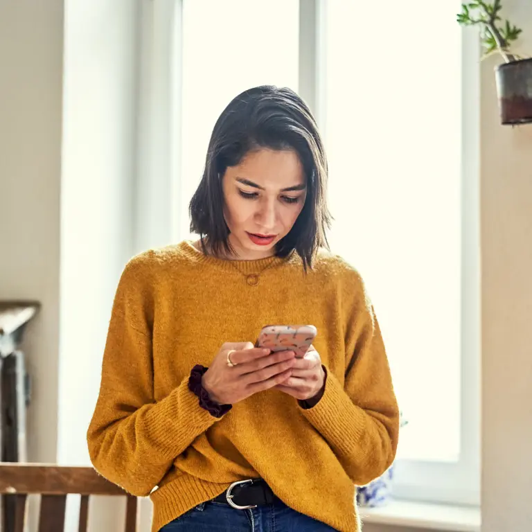 Frau hält Handy in der Hand und schaut runter auf das Display.