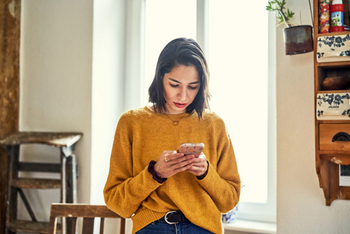 Frau schaut nach unten auf ihr Handy in ihrer Hand.