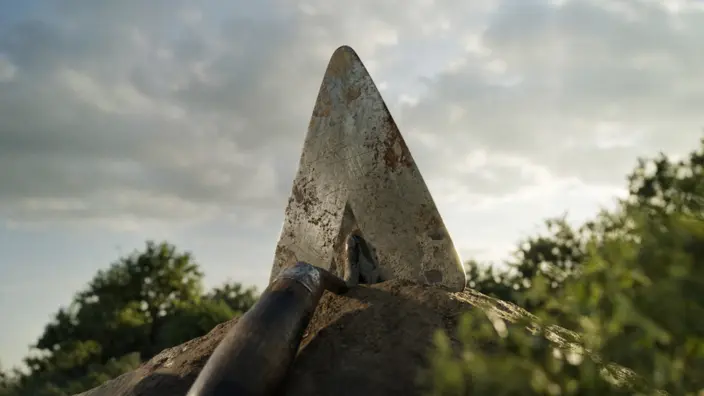 Maurerkelle liegt mit der SPitze nach oben auf einem Erdhaufen.
