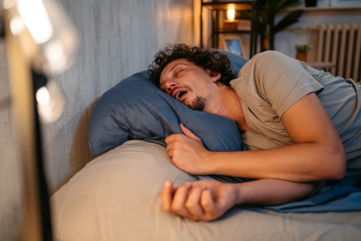 Mann schläft im Bett und sein Mund steht offen.