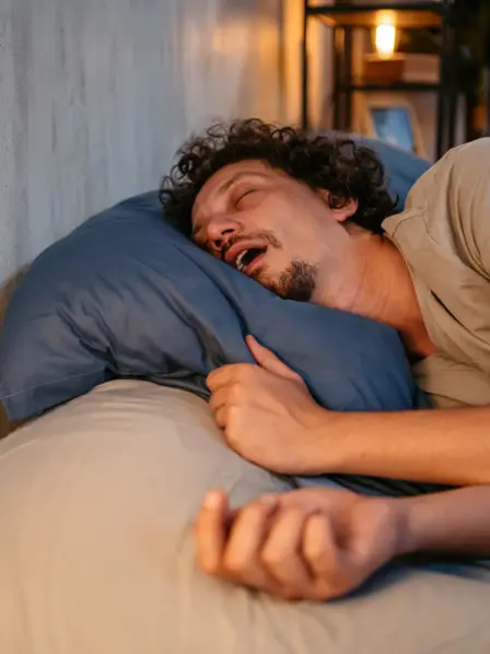 Mann schläft im Bett und sein Mund steht offen.