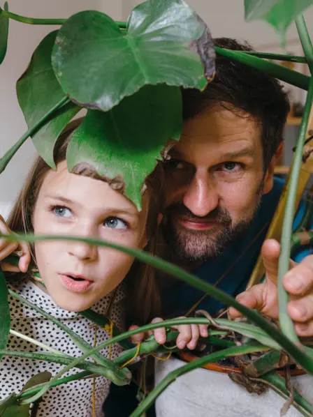 Vater und Tochter spielen hinter einen Zimmerpflanze, als seien sie im Dschungel.