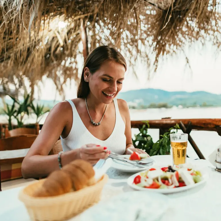 Frau isst im Urlaub in einem Restaurant am Meer.