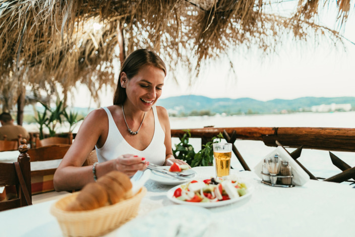 Frau isst im Urlaub in einem Restaurant am Meer.
