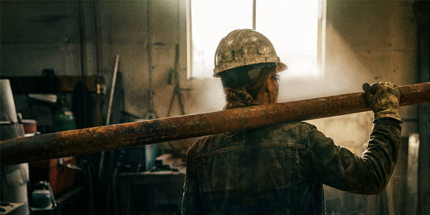 Handwerkerin trägt ein Stahlrohr auf ihrer Schulter.