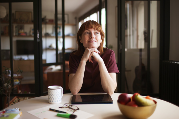 Frau sitzt mit zufriedener Miene am an einem runden Tisch in einer Wohnung. 