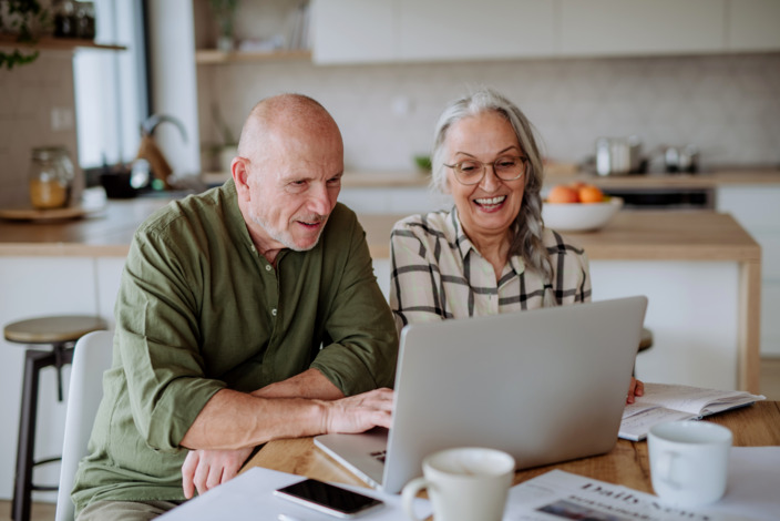 Senior und Seniorin schauen in einen Laptop.