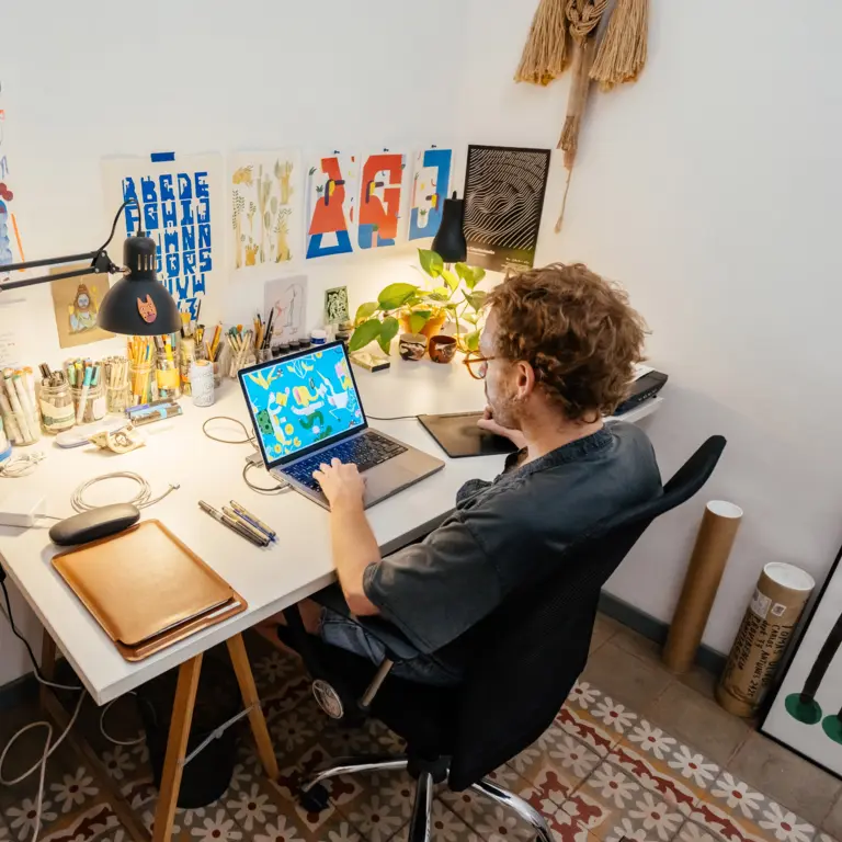 Grafiker sitzt an seinem Schreibtisch zu Hause und arbeitet am Laptop.