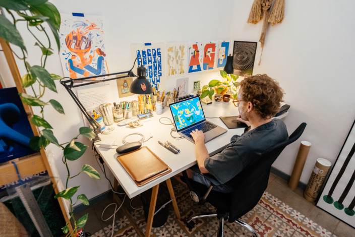 Grafiker sitzt an seinem Schreibtisch zu Hause und arbeitet am Laptop.
