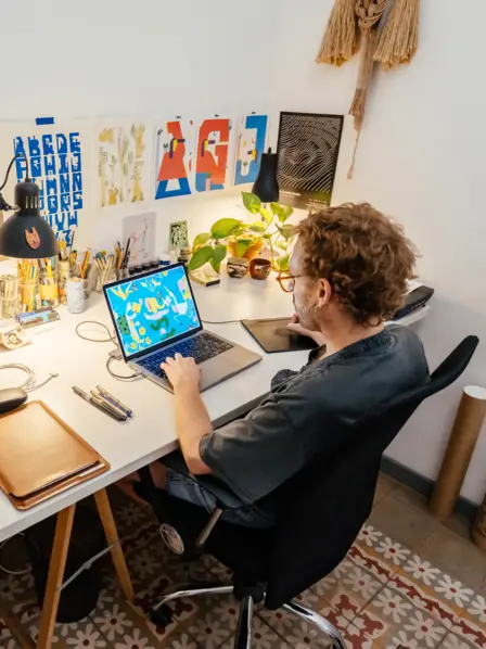 Grafiker sitzt an seinem Schreibtisch zu Hause und arbeitet am Laptop.