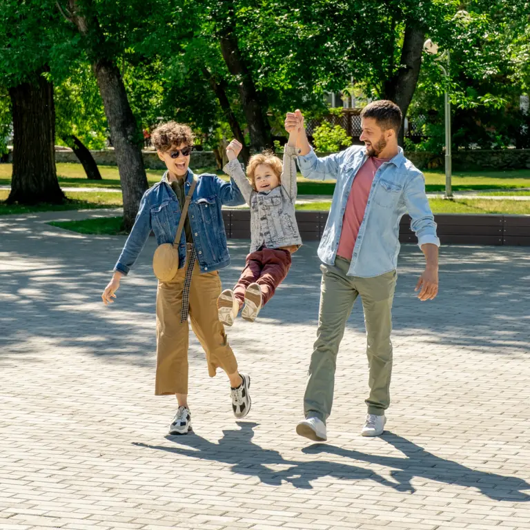 Mutter und Vater ziehen spielerisch in ihrer Mitte ihr Kind an den Armen nach oben.