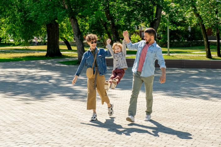Mutter und Vater ziehen spielerisch in ihrer Mitte ihr Kind an den Armen nach oben.
