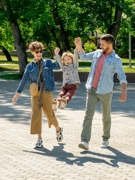 Mutter und Vater ziehen spielerisch in ihrer Mitte ihr Kind an den Armen nach oben.