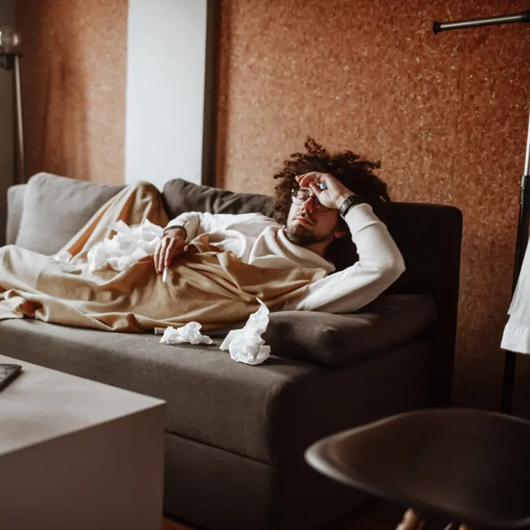 Kranker Mann liegt auf dem Sofa unter einer Decke.