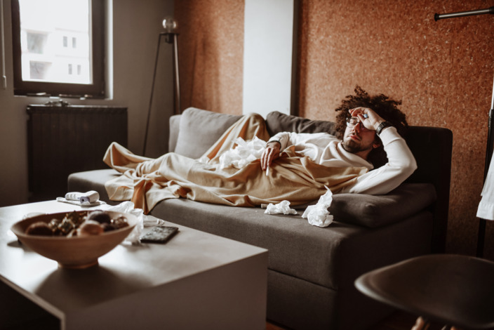 Kranker Mann liegt auf dem Sofa unter einer Decke.