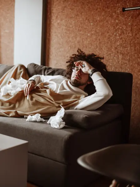Kranker Mann liegt auf dem Sofa unter einer Decke.