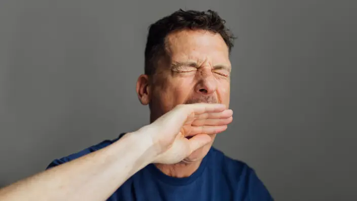 Mann hält sich beim Gähnen die Hand vor den Mund