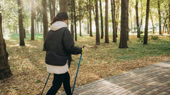 Frau läuft mit Walking Stöcken durch einen Wald.